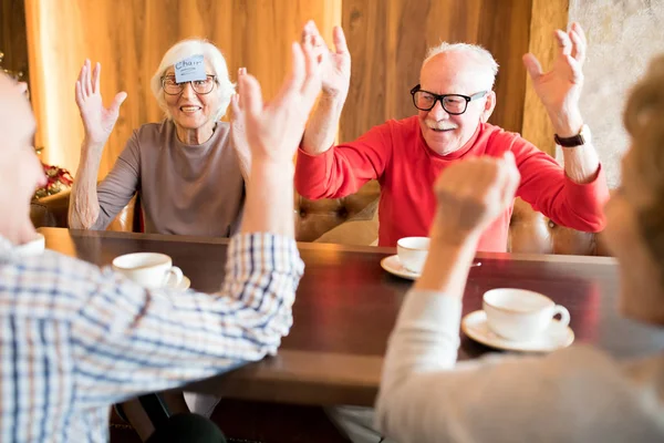 ポジティブ興奮した先輩がカフェのテーブルに座り 単語推測ゲームをしながら握手をする — ストック写真