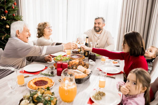 Warm-toned portrait of big happy family enjoying Christmas dinner together and clinking glasses