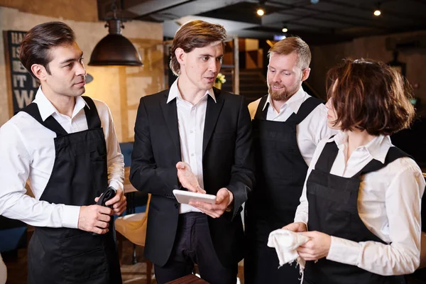 Content confident handsome young manager pointing at tablet screen while assessing work of waiters and explaining their mistakes