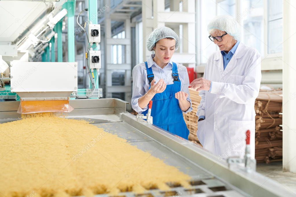 Portrait of two women discussing production  standing by conveyor belt at modern  food factory, copy space