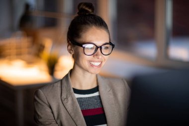 Karanlık ve mesai içinde otururken bilgisayar ekranına bakarak gülümseme dişlek ile neşeli ofis Müdürü