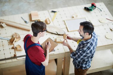 Doğrudan gömlek ayakta marangozluk Danışma ve ahşap ayrıntılı notlar eskiz defteri içinde yapım genç meslektaşım için gösterilen ciddi orta yaşlı adam görünümünü yukarıda kareli.
