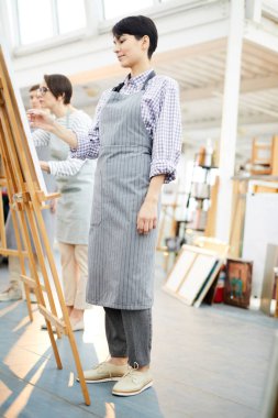 Sanat stüdyosunda şövale üzerinde modern genç kadın boyama resmi tam uzunlukta yan görünüm portre