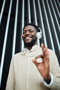 Neşeli genç adam beyaz kazaklı Tamam işareti için kulaklık müzik dinlerken gösterilen