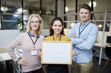 Modern ofiste duran rozetleri ve boş afiş, takım kavramını kullanarak projeyi sunan pozitif güvenilir ofis meslektaşları