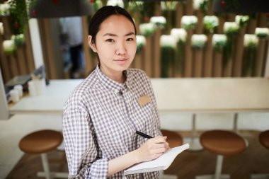 Güzel genç Asyalı kadın gömlek veya iş kıyafeti size bakarak Not defteri 'nde sipariş aşağı yazarken