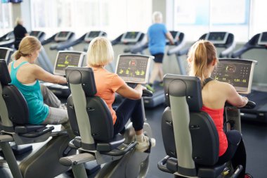 Spor salonunda ki spor salonunun önünde fitness bisikletleri üzerinde oturan ve antrenman yapılan olgun aktif sporculardan oluşan bir grup
