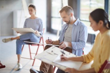 Stüdyoda oturan ve skeçler kağıtlara yapma Sanat Okulu çağdaş öğrenenler grubu