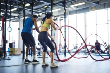 Çapraz eğitim merkezinde halat savaşı uygulayan aktif giyimli kültürlerarası erkek ve kadının geri görünümü