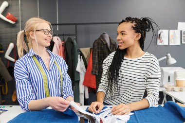 İki genç moda tasarımcısı birlikte işyeri yakınında duran ve atölyede yeni elbise üzerinde çalışırken gülümseyerek