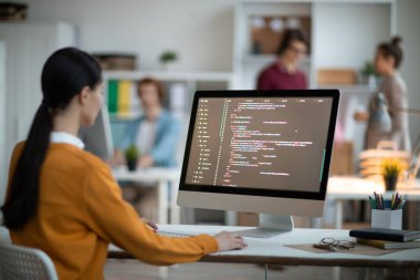Genç kadın programcı tarafından Danışma bilgisayar ekranı önünde oturan ve analiz gündelik giysiler içinde veri kodlanmış