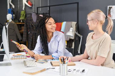 Ofis masasında oturan iki kadın tasarımcı renkli palet ve bilgisayarla çalışarak gelecek planlarını tartışıyor
