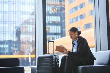 Havaalanı penceresinde oturan genç bir iş gezgini defterinde müşteri numarasını arıyor.
