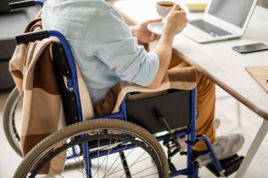 Resepsiyon ve sahip çay veya kahve dizüstü bilgisayar önünde oturup tekerlekli sandalye üzerinde işadamı