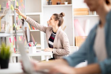 Genç kadının önünde bilgisayar monitörü Masası tarafından otururken göstermek çalışma notları gösteren