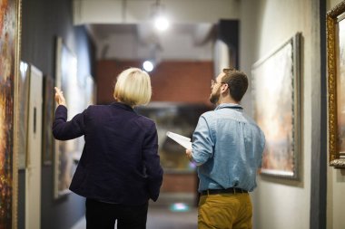 Back view portrait of two museum workers discussing paintings walking in art gallery, copy space clipart