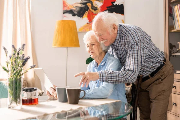 Side view portrait of modern elderly couple using laptop at home while online-shopping together, copy space
