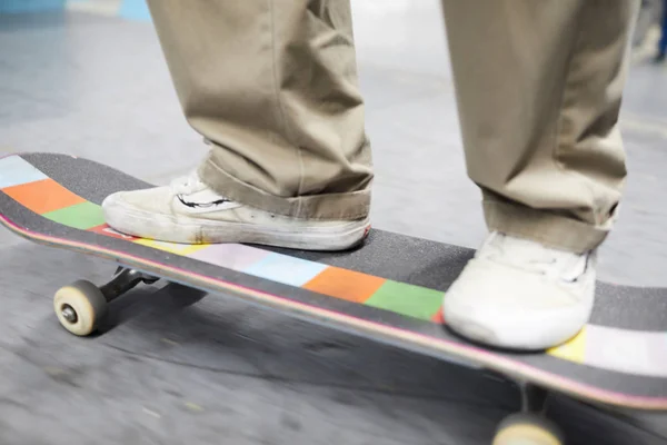 Human legs in casual pants and sportive footwear standing on skateboard while moving down flat surface