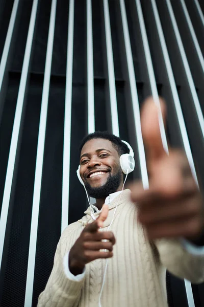 快乐的非裔美国人在休闲服装指着你 而享受耳机中的音乐 — 图库照片