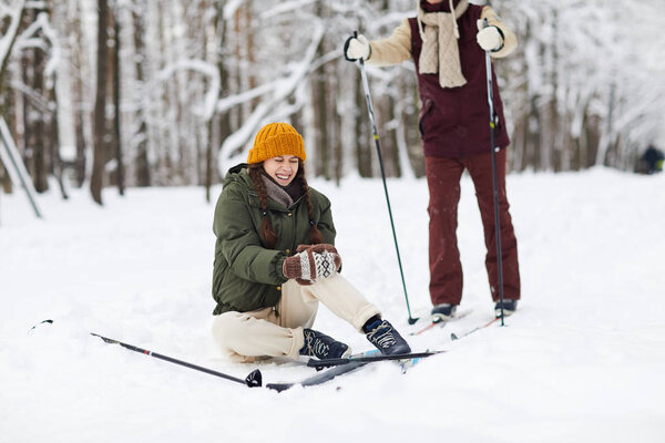 Full length portrait of crying young woman sitting on snow injured during skiing, copy space