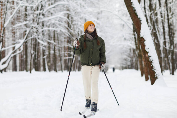 Full length portrait of active young woman skiing alone in beautiful winter forest enjoying nature, copy space