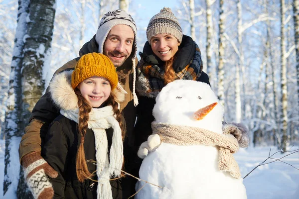 腰起幸福的家庭建设雪人在冬季森林和微笑在相机 复制空间的肖像 — 图库照片