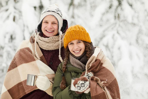 在美丽的冬季森林里享受徒步旅行时 用毯子包裹着活跃的年轻夫妇的肖像 在户外喝着热可可 复制空间 — 图库照片