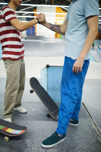 パルクールスタジアムに立ちながら 友情とサポートの象徴として握手をするカジュアルウェアの2人の若いスケートボーダー — ストック写真