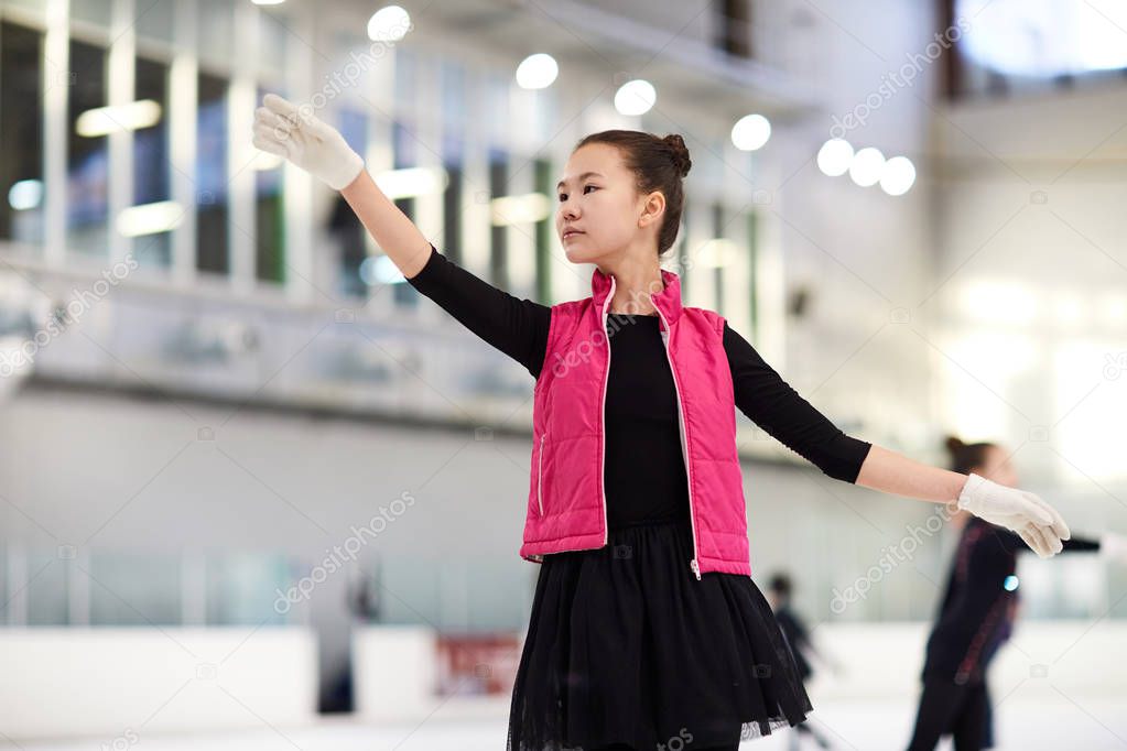 Waist up portrait of graceful Asian girl figure skating on ice rink and looking away dreamily, copy space