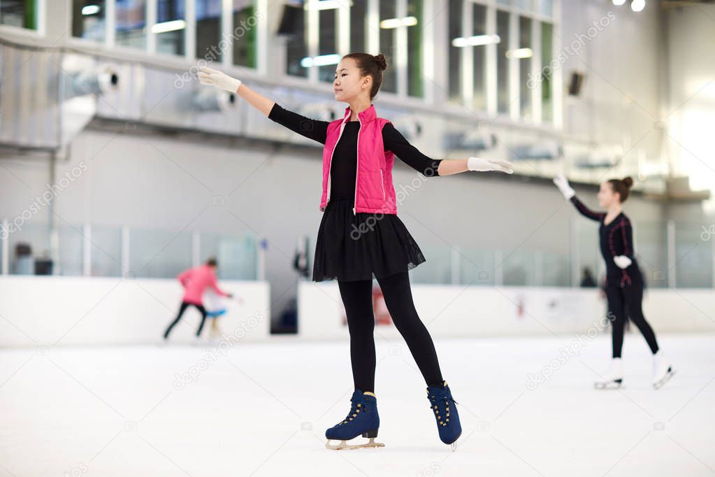 Full length portrait of graceful Asian girl figure skating on ice rink and looking away dreamily, copy space