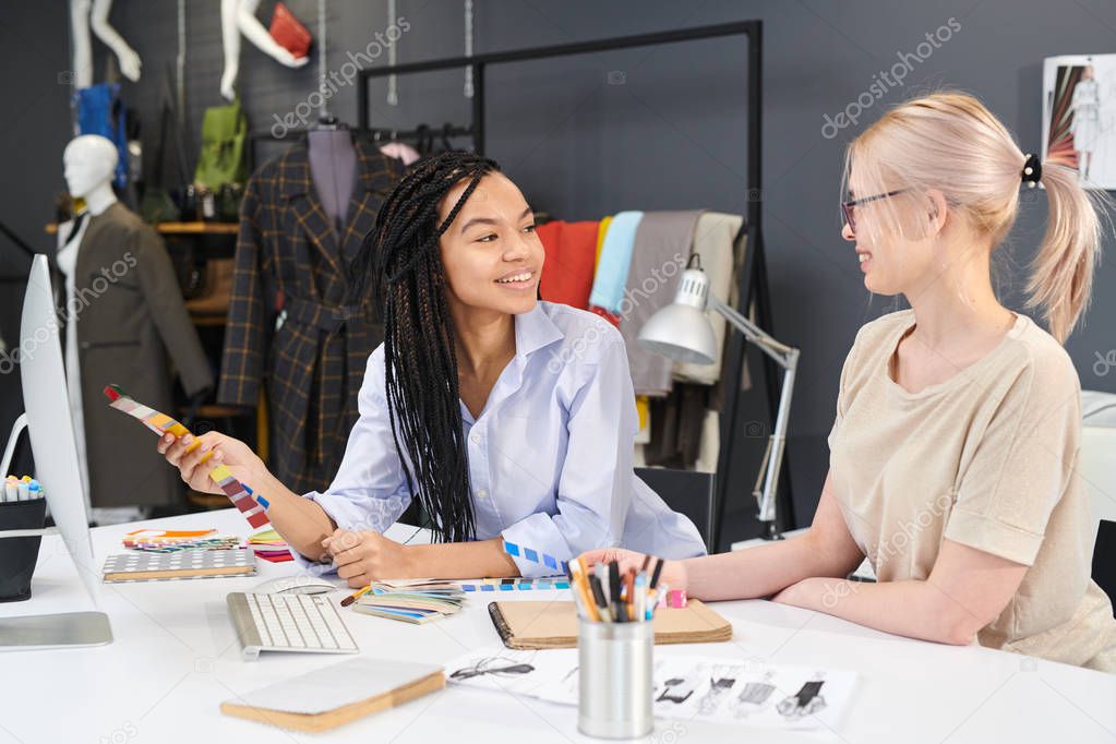 Two female designers sitting at office table working with colorful palette and computer and discussing their future plans