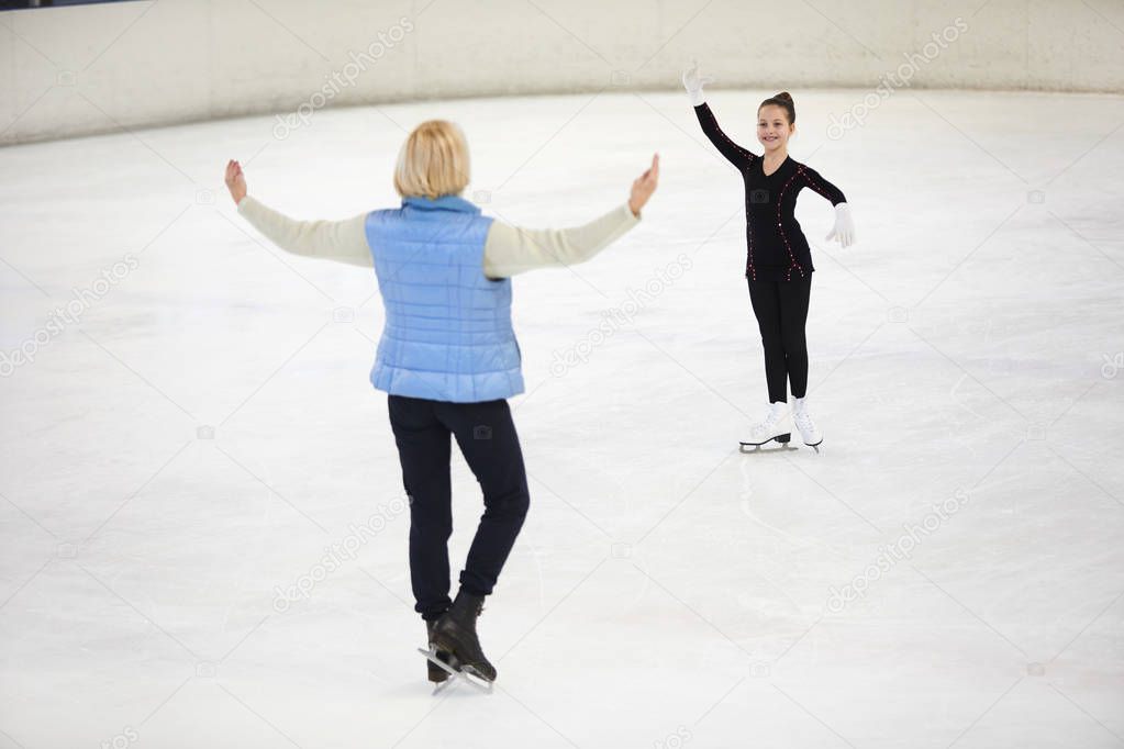 Full length portrait of happy girl figure skating on rink with female coach giving instructions, copy space