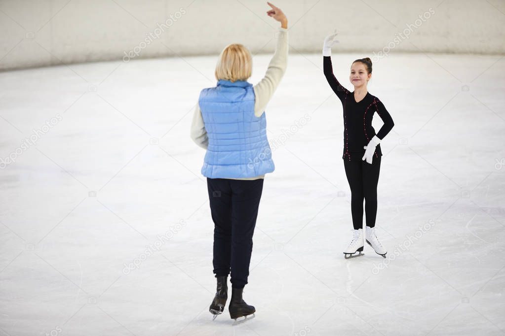 Full length portrait of smiling girl figure skating on rink with female coach giving instructions, copy space