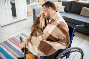 Depresif genç adam ekose yüz ve şişe şarap ve diğer bir yandan ile tekerlekli sandalyede oturan sarılmış devre dışı