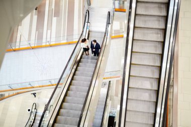 Harika insanlar iki genç çalışanın genel bakış yürüyen merdiven üzerinde hareket ve büyük modern ticaret merkezi içinde konuşurken