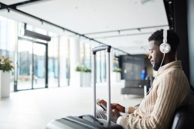 Havaalanı lounge alanında oturup ve uçuş için beklerken smartphone içinde kaydırma kulaklık rahat iş adamı
