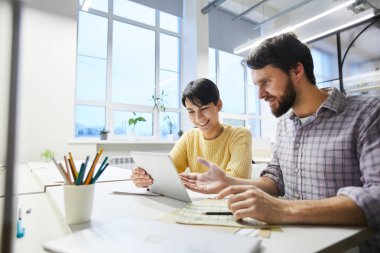 Ofiste modern tablet kullanırken rahat giyim masada oturan ve İnternet projesi tartışarak olumlu heyecanlı genç meslektaşları