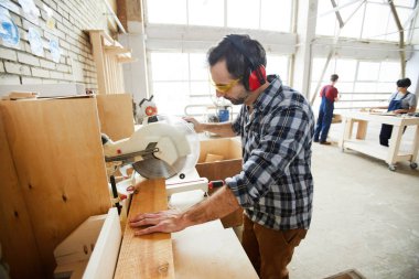 Ayakta tezgah ve daire testere ile kesme ahşap parça ciddi konsantre yakışıklı orta yaşlı adam kulak koruyucular ve koruyucu gözlükler