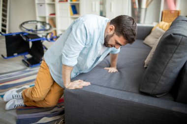 Genç adam yerden kanepede tekerlekli sandalye düştükten sonra ayağa kalkmaya çalışırken gündelik giysiler içinde devre dışı