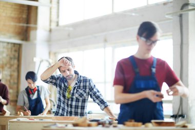 Masada duran ve alin ahşap parça bakarken sürtünme anız ile düşünceli şaşkın orta yaşlı marangoz
