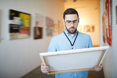 Waist up portrait of pensive bearded man holding picture in art gallery or museum, copy space clipart