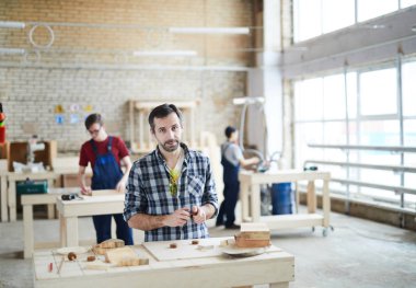 İçerik yakışıklı orta yaşlı marangoz ahşap detayları ile masada duran ve çocuklar oyuncak montaj sırasında kameraya bakarak Kareli gömlekli