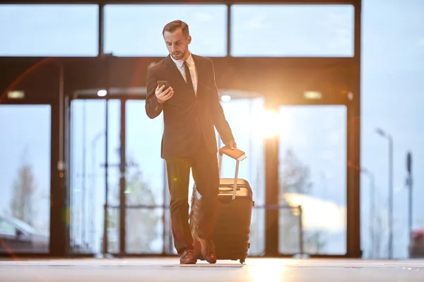 Jonge Elegante Zakenman Trekken Koffer Tijdens Het Scrollen Smartphone Voor — Stockfoto