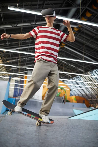 パルクールエリアでスケートボードしながら バーチャルリアリティで旅行カジュアルウェアの十代の男 — ストック写真