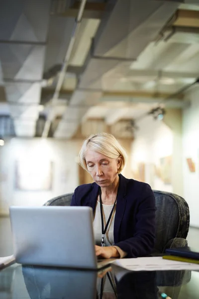 Portrait of mature businesswoman using laptop at workplace in modern gallery or museum