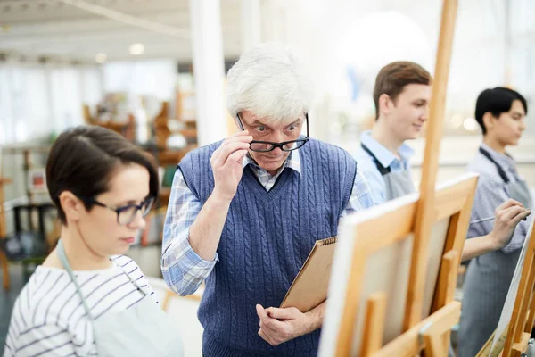 成熟した芸術教師の肖像美術クラスのイーゼルの学生の絵の仕事を批判する作品 コピースペース — ストック写真