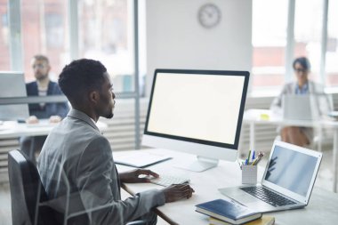 Young confident broker looking at computer screen while searching for online data for his project or presentation