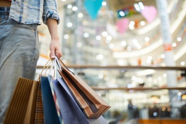 Alışveriş merkezinde alışveriş poşetleri taşıyan kot pantolonlu kimliği belirsiz kadının yakın çekim, tek başına alışveriş yapıyor