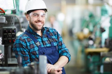 Waist up portrait of bearded factory worker wearing hardhat smiling at camera while posing in workshop, copy space clipart