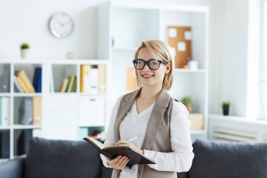 Ofisin içinde kameranın önünde dururken not defterine not alan başarılı genç bir psikolog.